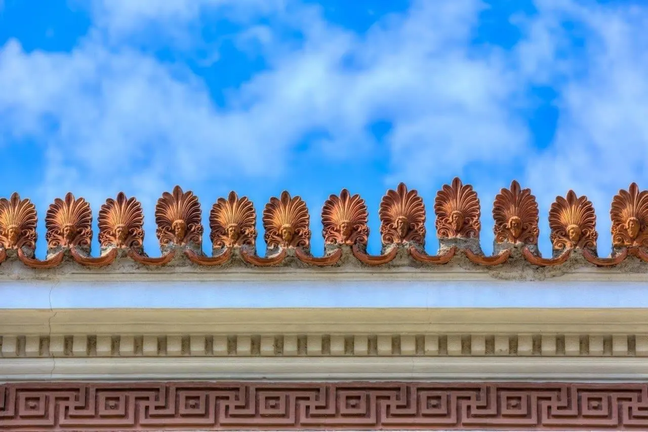 A row of terracotta roof ornaments above a Greek key frieze