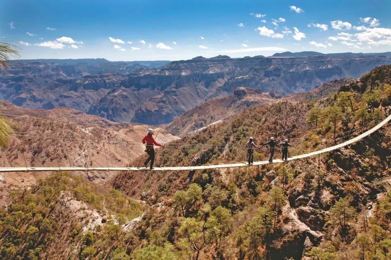 Walkers crossing a long suspension bridge high above the Copper Canyon