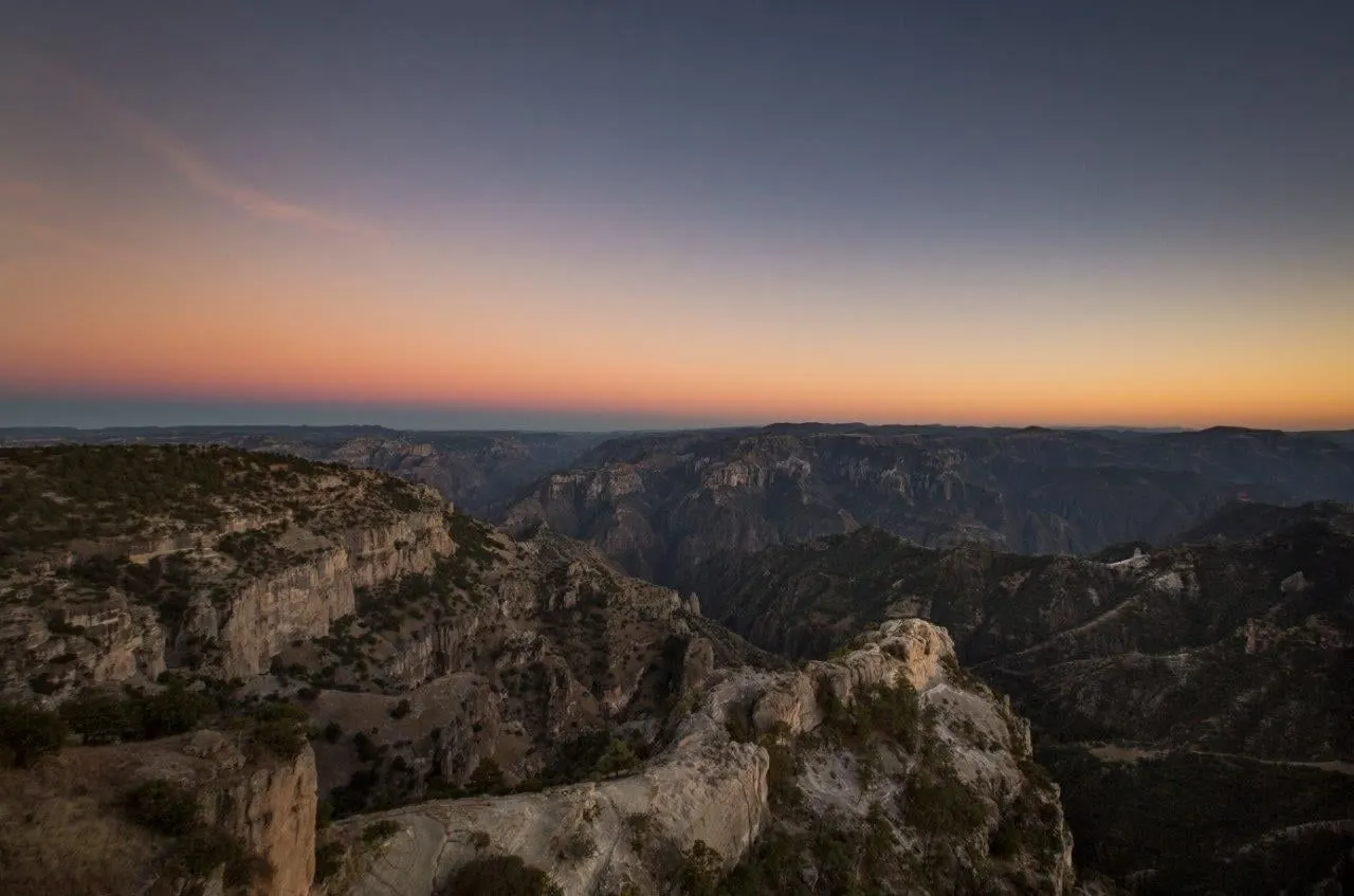 Layered ridges of the Copper Canyon under an orange sunset sky