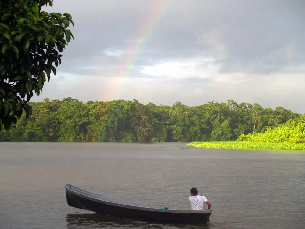 A wooden canoe on a jungle river beneath a faint rainbow