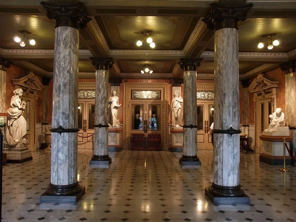 An ornate theatre foyer with marble columns and statues