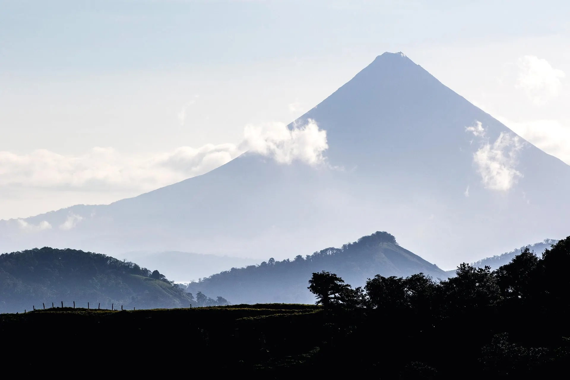 A volcano peak rising above misty hills and low cloud