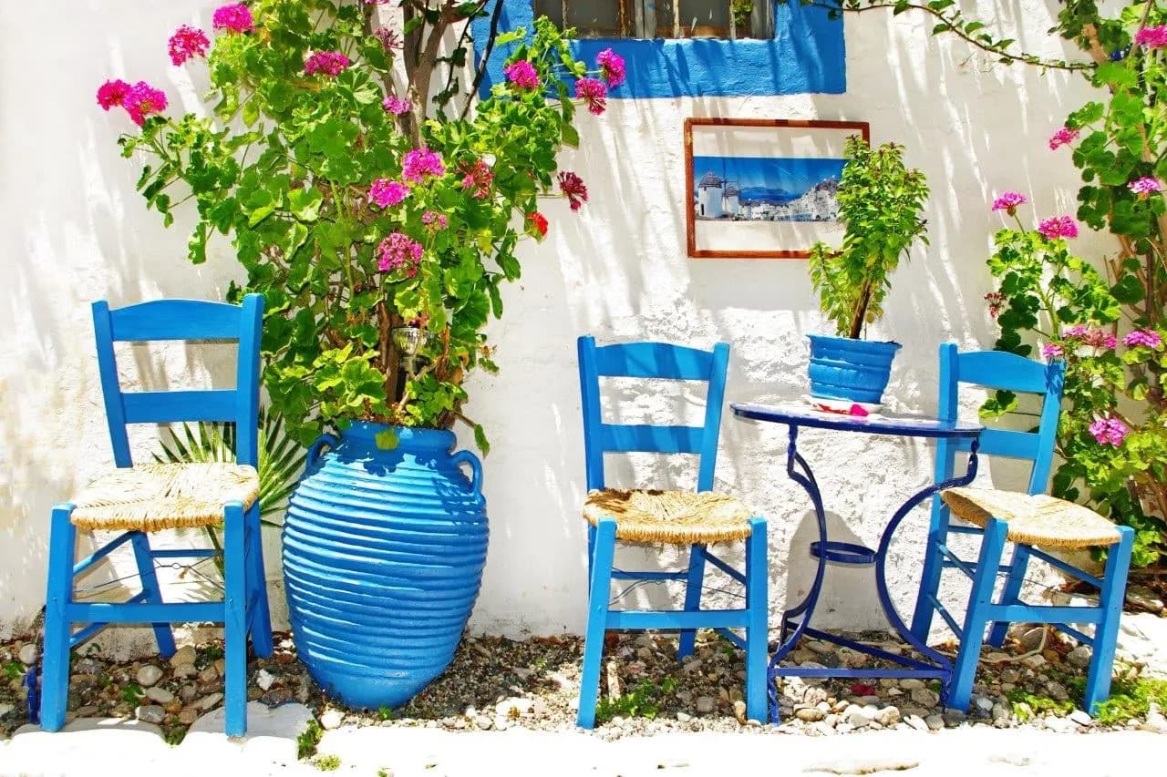 Blue chairs and a blue clay pot against a whitewashed wall with pink flowers