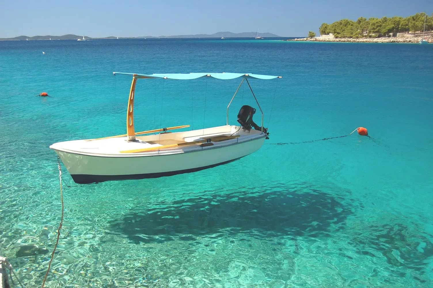 A small white boat floating on clear turquoise water off an island
