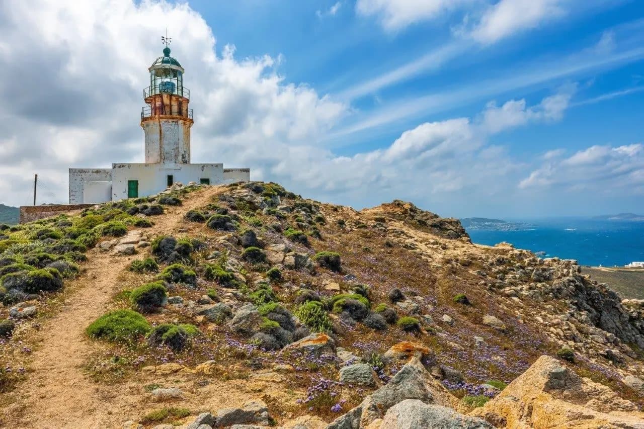 A white lighthouse on a rocky headland above the Aegean