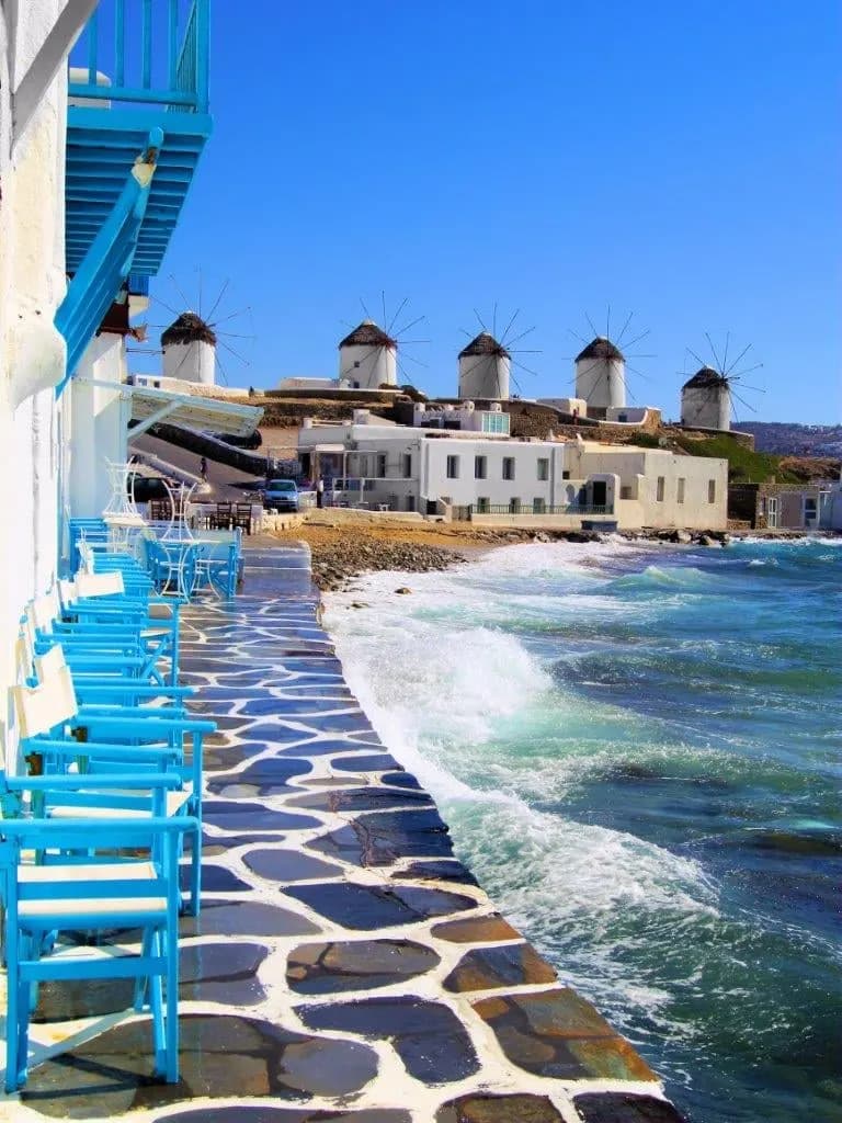 Blue chairs on a waterfront terrace looking across to the Mykonos windmills