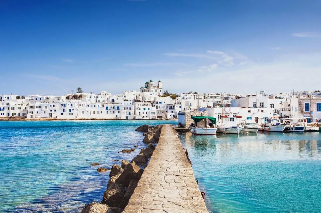 A whitewashed island town across a turquoise harbour with a stone breakwater