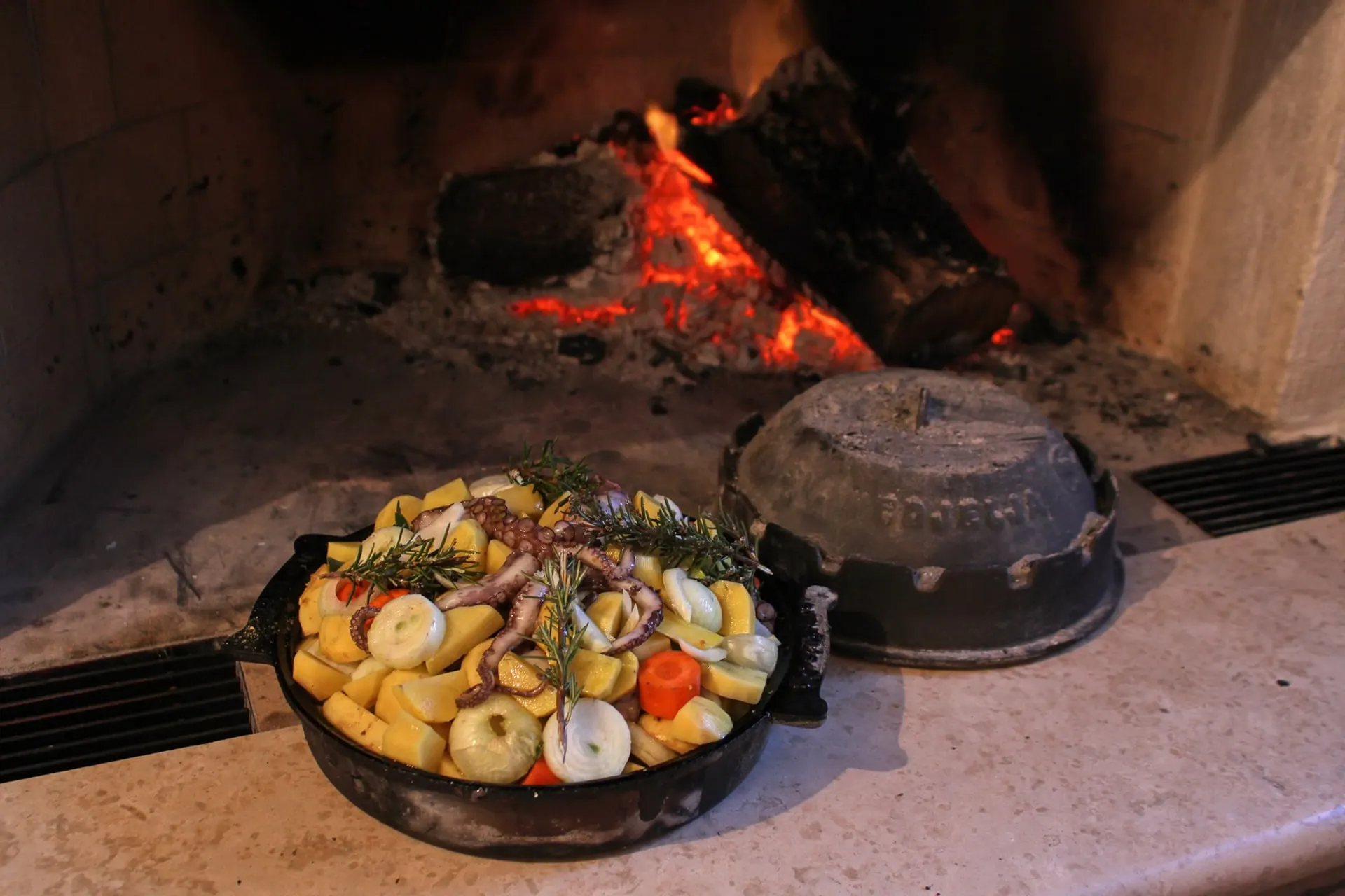 A peka dish of meat and vegetables beside a wood fire