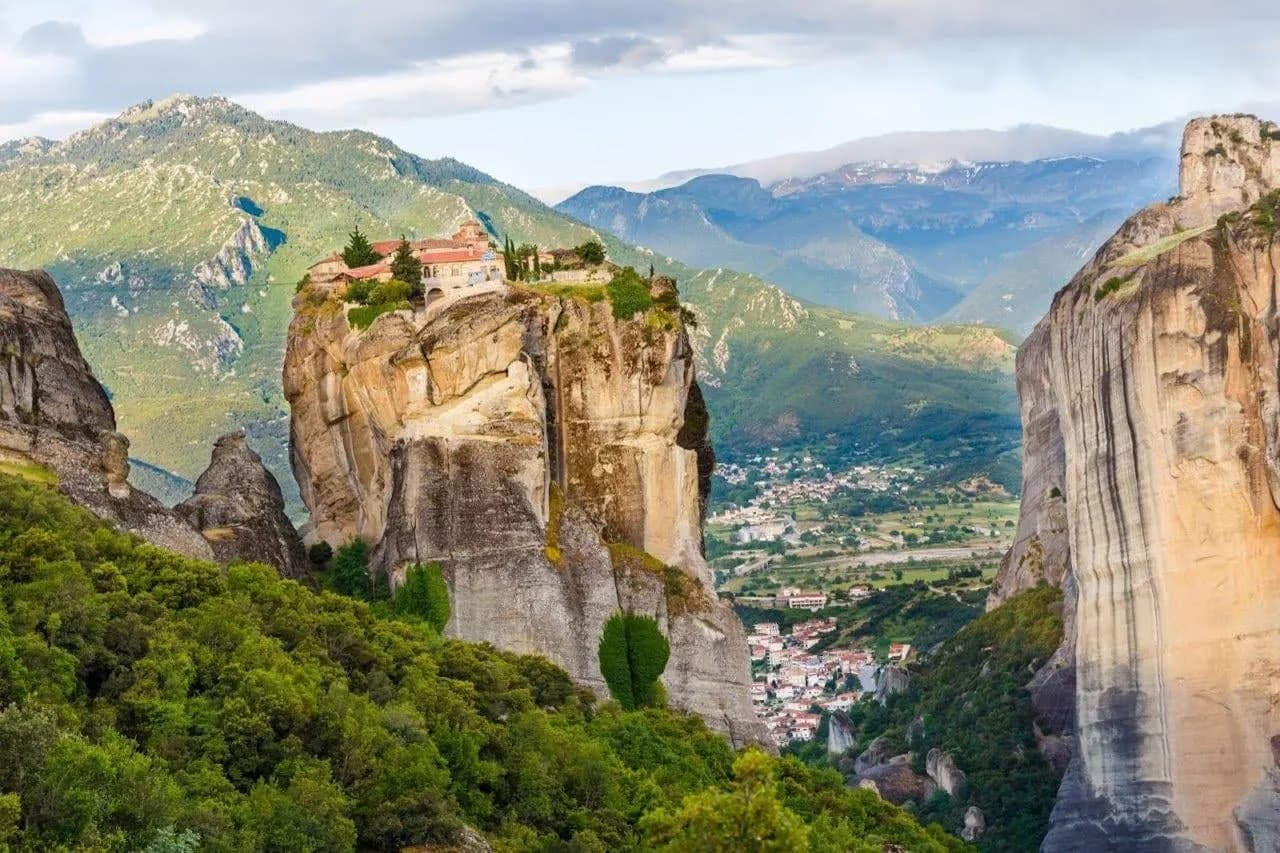 A monastery on top of a sandstone tower at Meteora, with the valley and town below