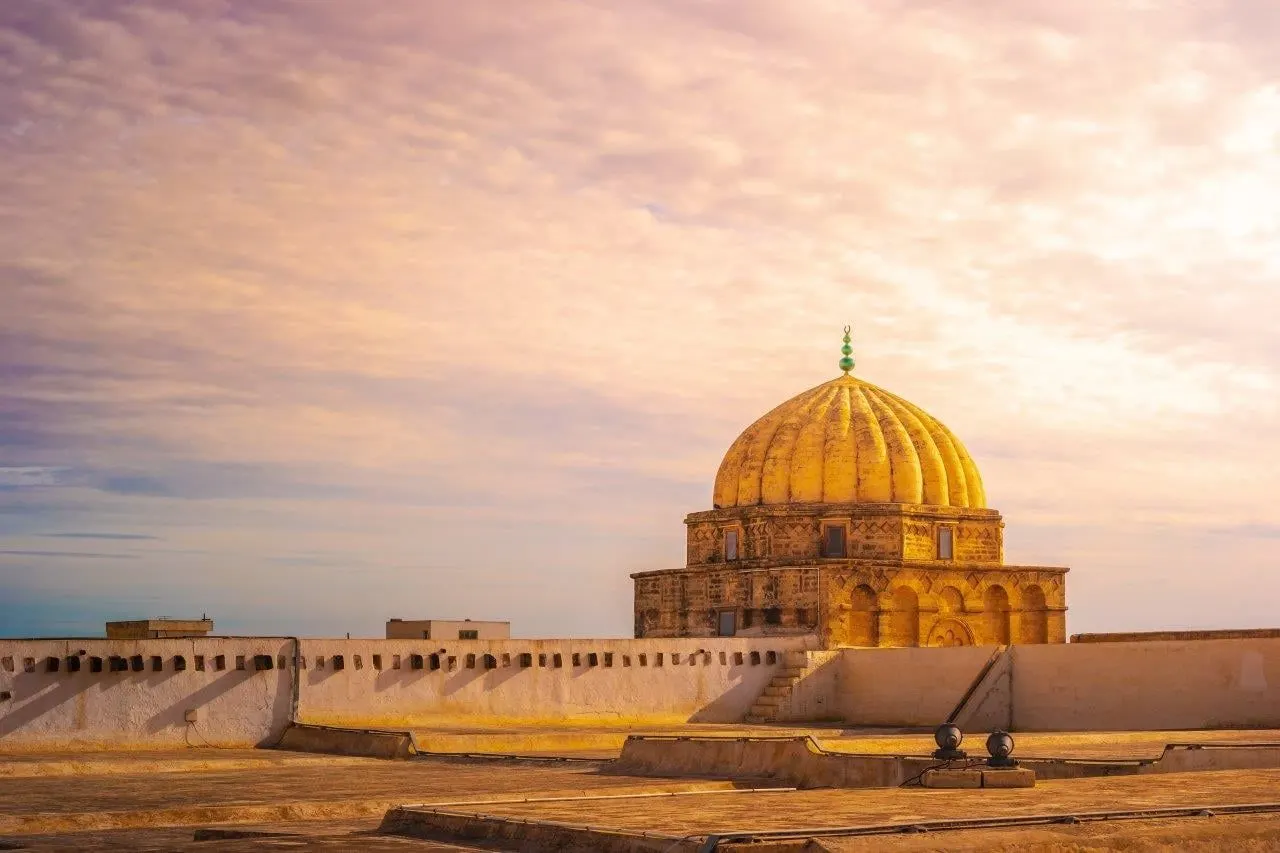A golden ribbed dome above old walls in the glow of sunset