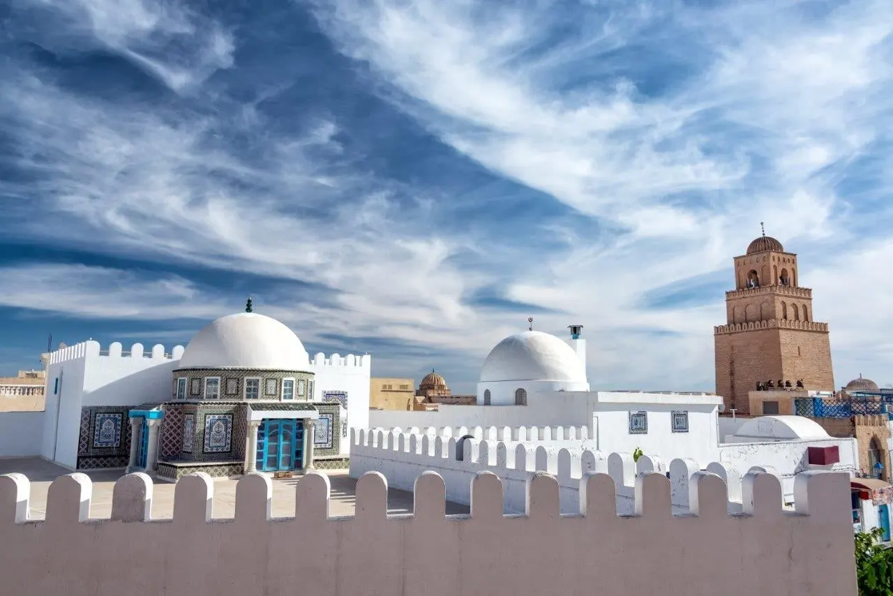 White domes and a square minaret behind crenellated walls under a wide sky