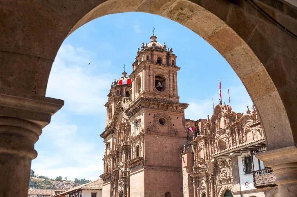 A baroque church tower on the Cusco main square seen through a stone arch