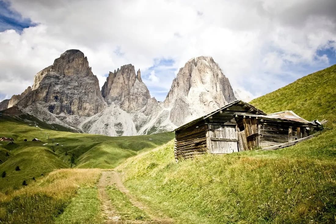 An old wooden hut on an alpine meadow below three rocky Dolomite peaks