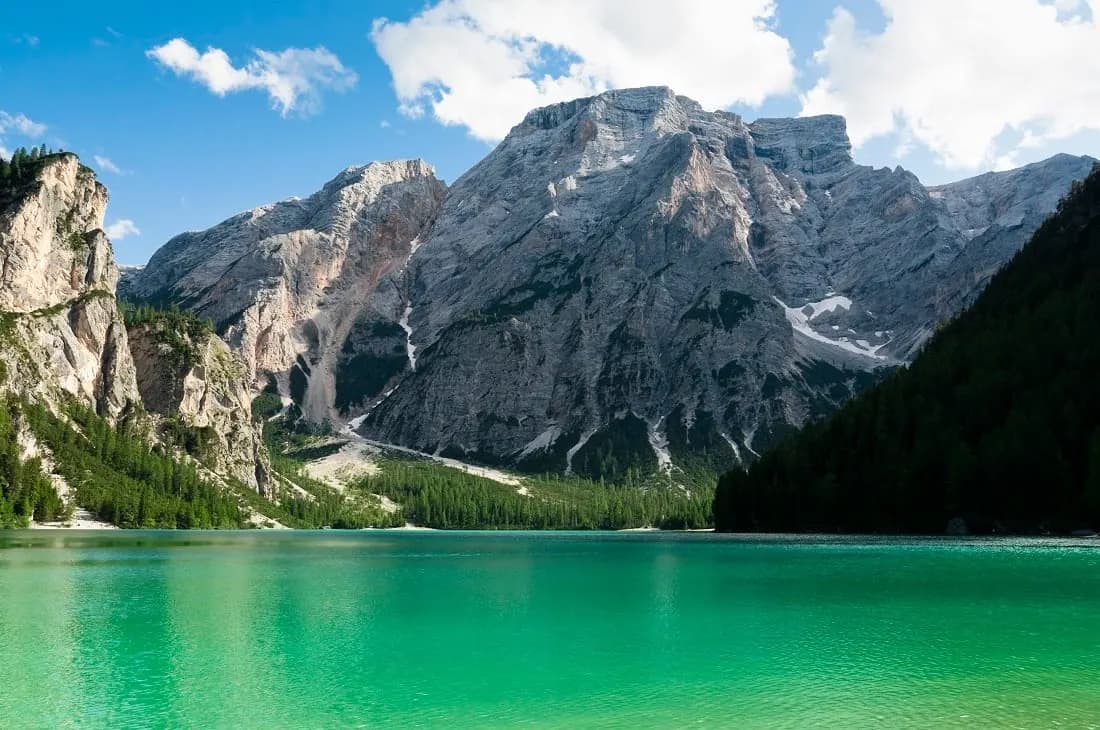 Turquoise water of Lake Braies below grey limestone mountains and pine forest