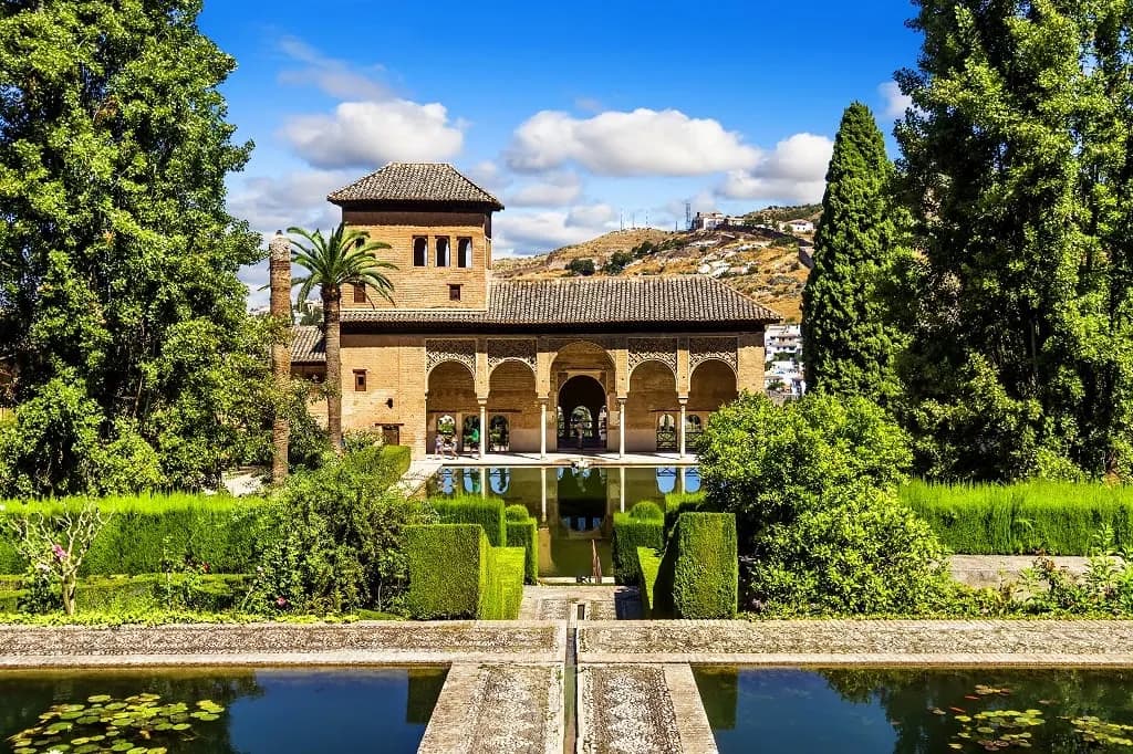 A palace pavilion behind clipped hedges and a pool in the Alhambra gardens