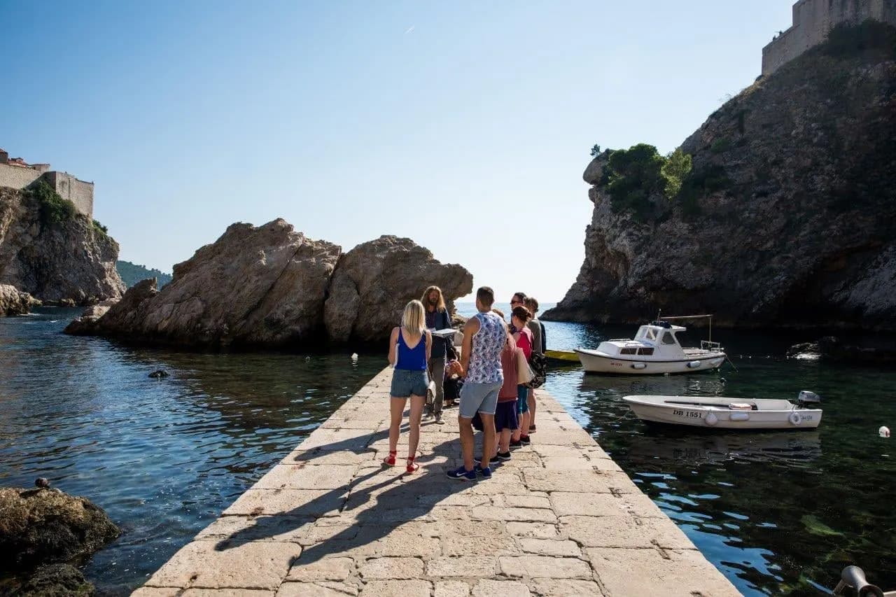 Visitors walking a stone pier in a sheltered cove below the fortress walls