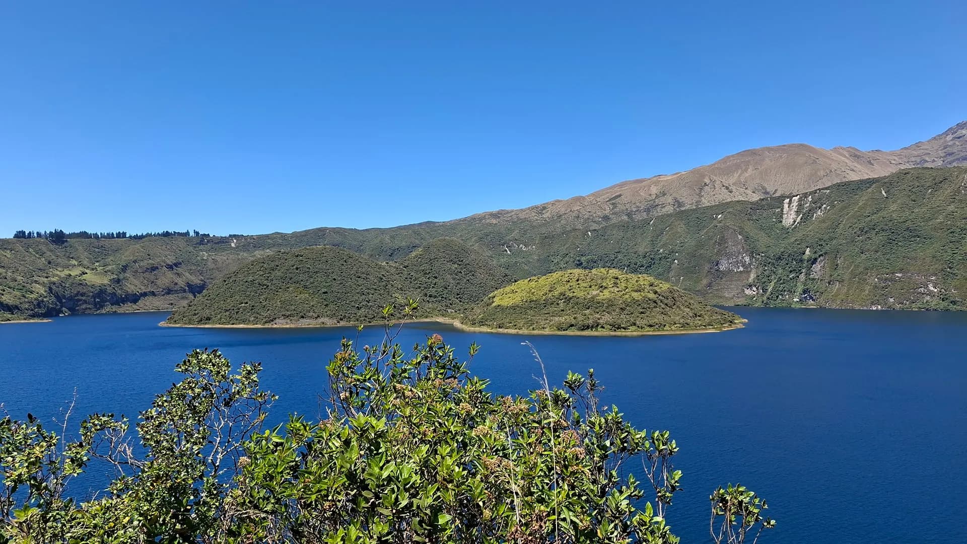 A deep blue crater lake with a green island in the middle