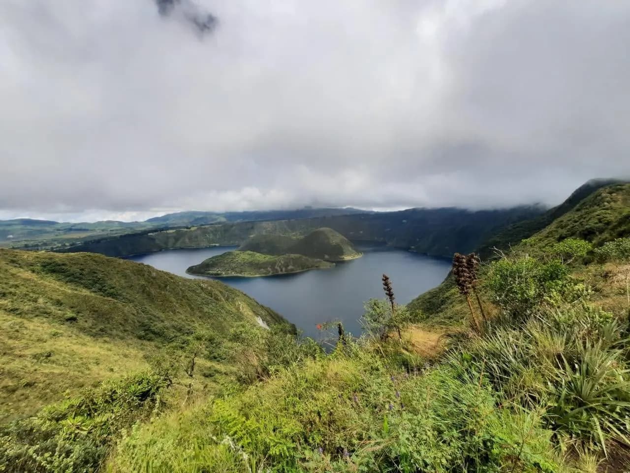 Green hillsides above a crater lake under low cloud