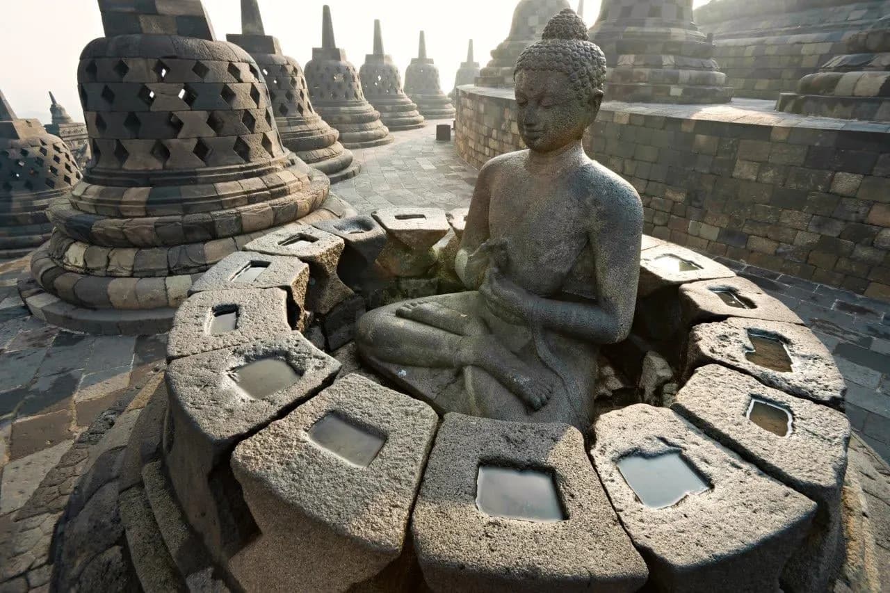 A stone Buddha among the latticed stupas on the upper terrace of Borobudur