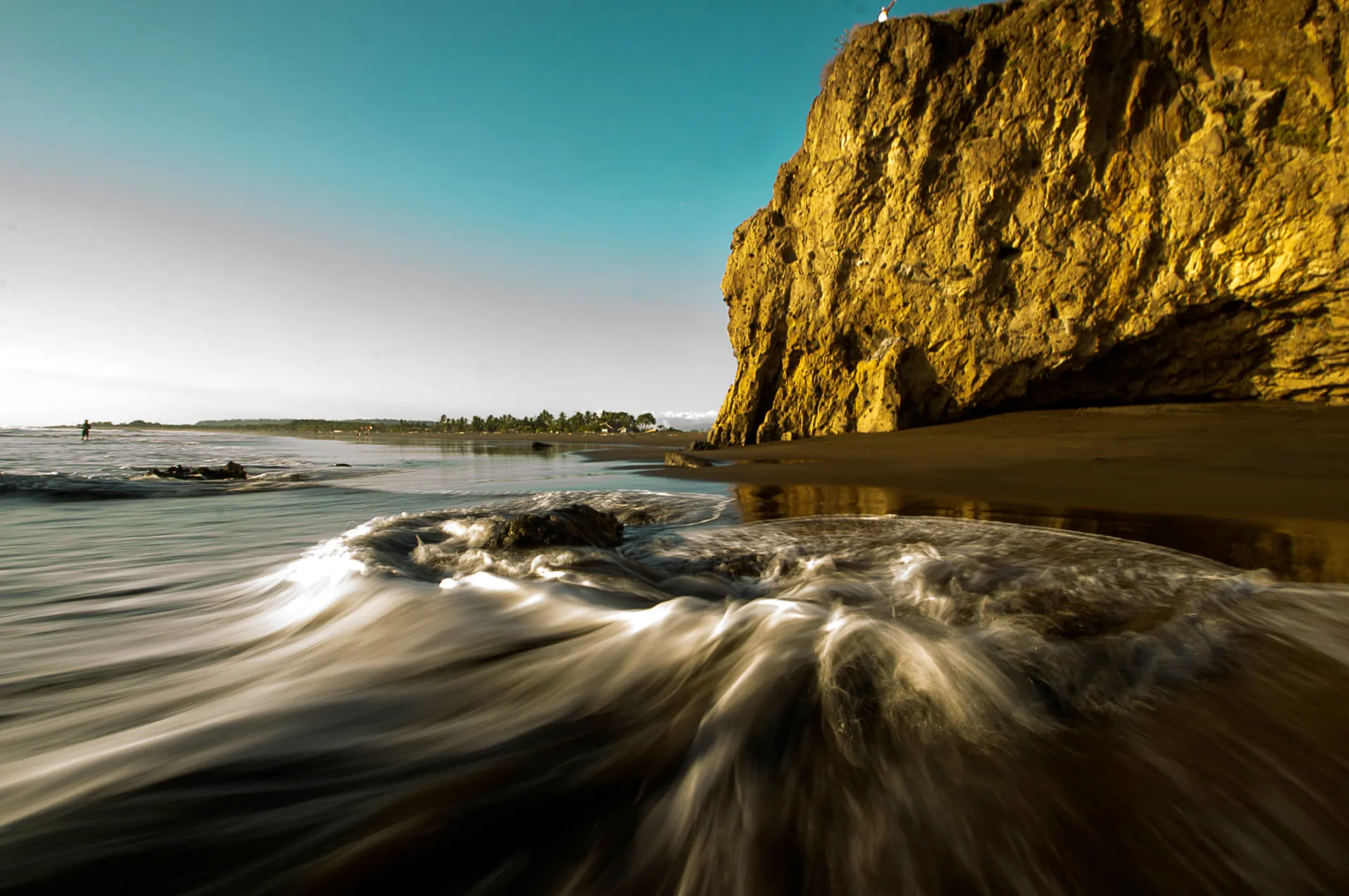 Waves washing over rocks below a golden sea cliff
