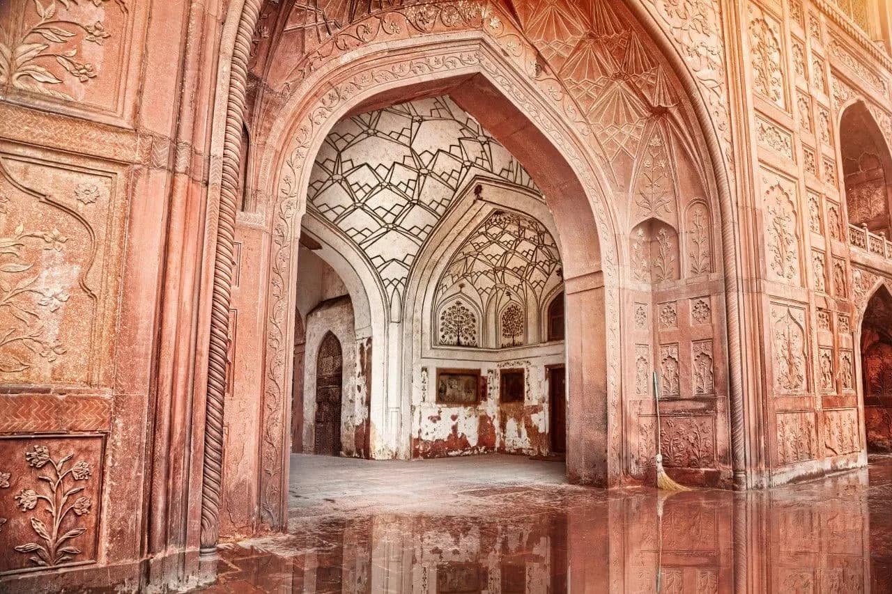 Carved sandstone arches reflected on a polished floor inside a Mughal fort