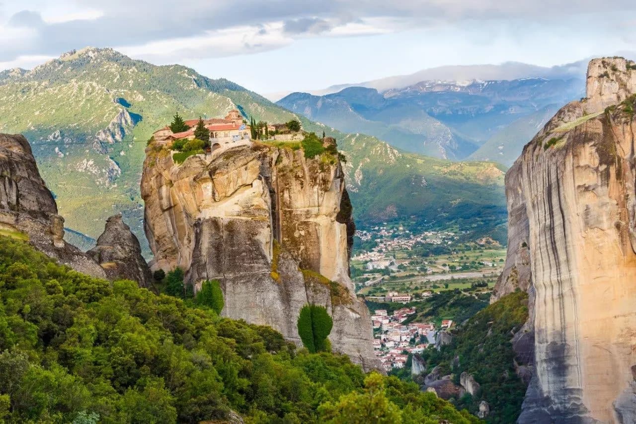 A monastery on a rock tower at Meteora, with green mountains beyond