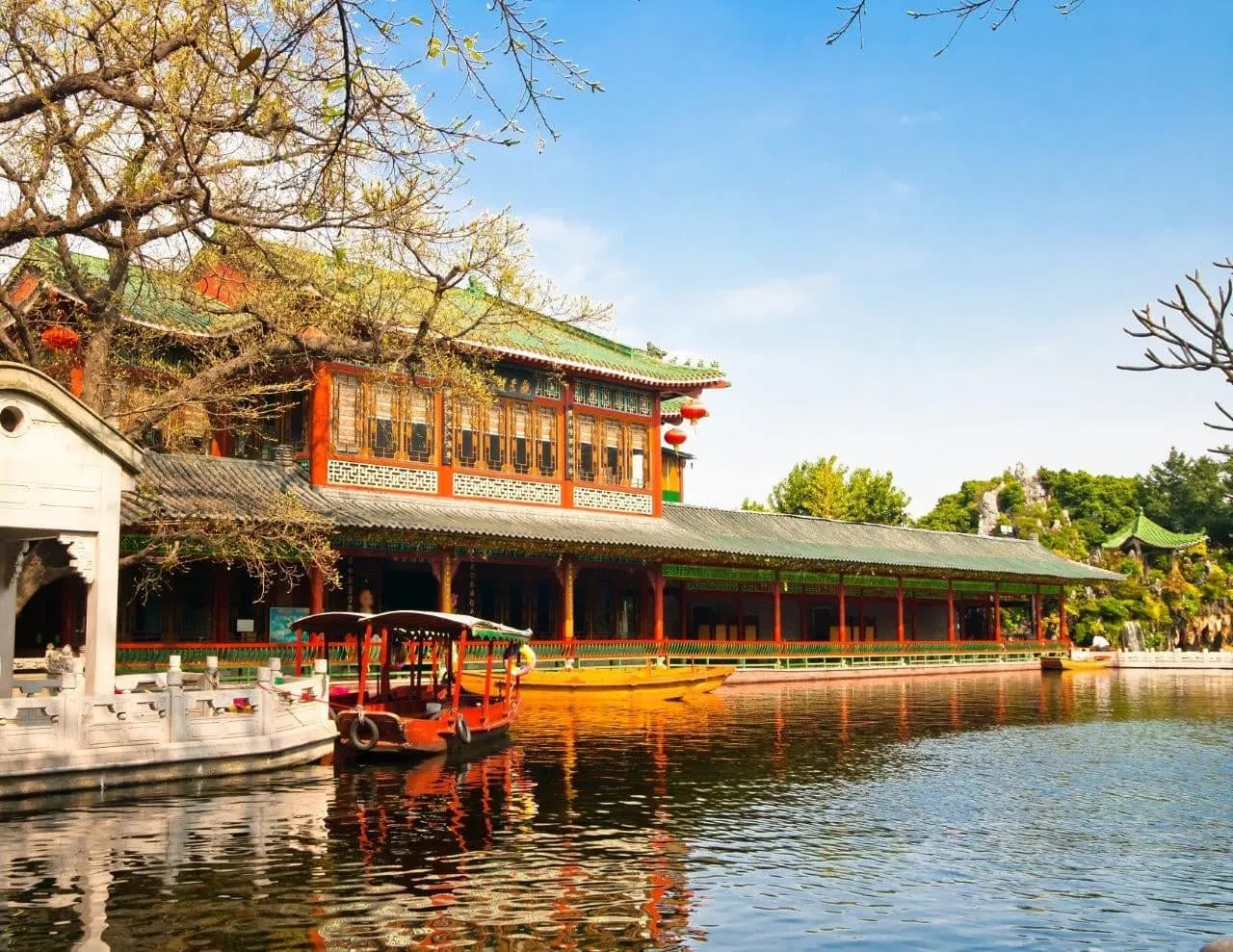 A painted boat on a garden lake in front of a long red pavilion