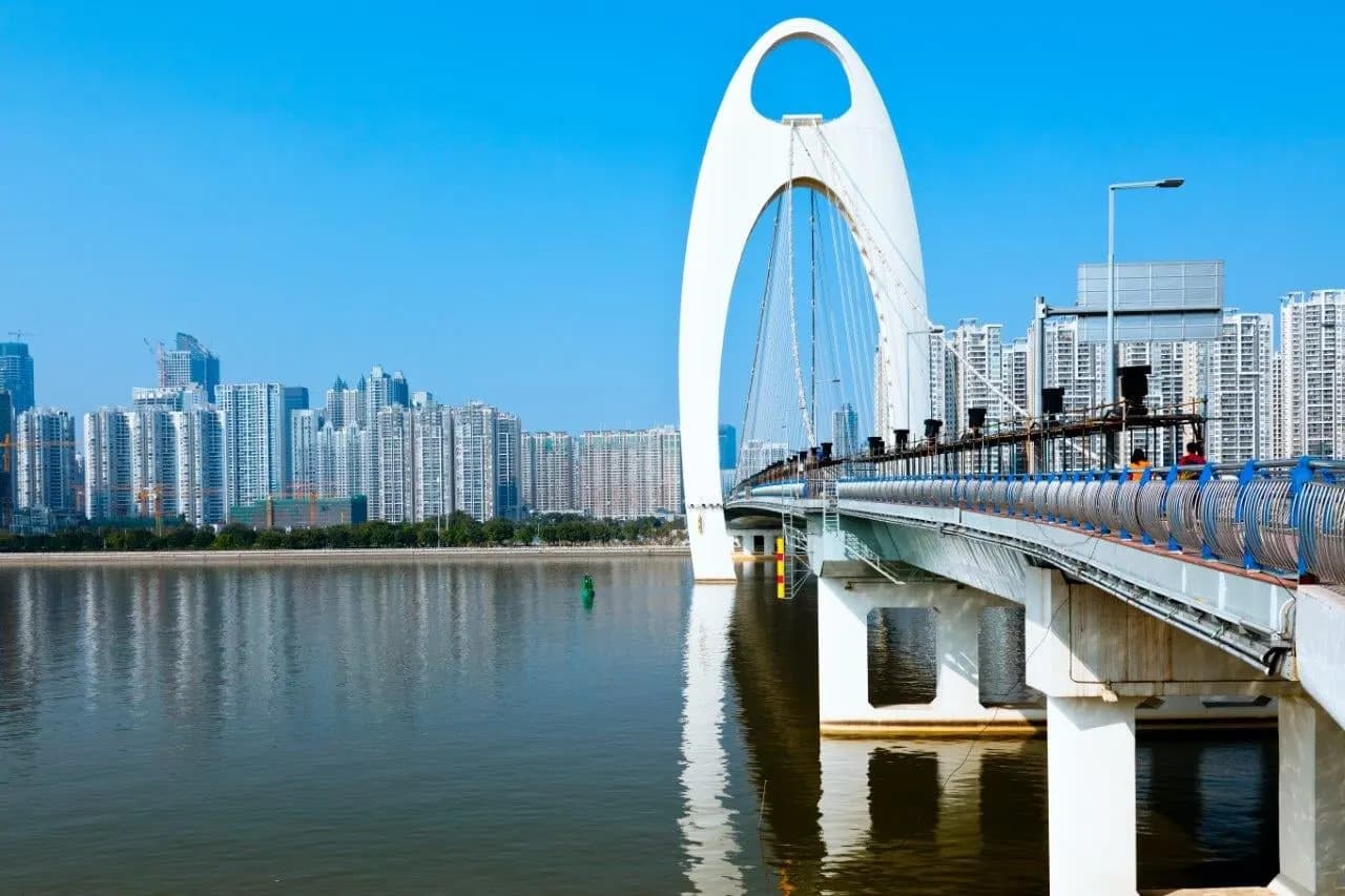 A white arched bridge spanning the Pearl River in front of high-rise towers