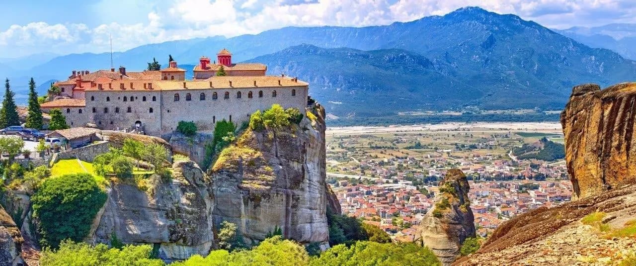 A Meteora monastery on a rock above the plain, with mountains behind