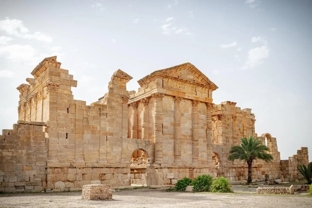 The tall stone walls of a Roman temple with a palm tree in front
