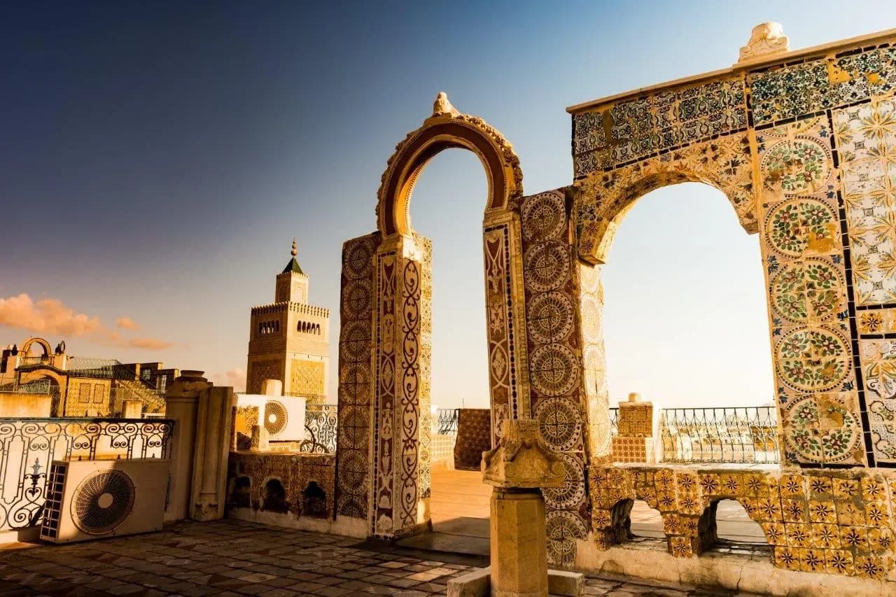 Tiled arches on a medina rooftop with a minaret beyond