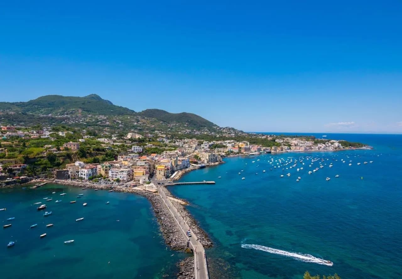 Looking along Ischia's coast to a stone causeway and boats in the bay