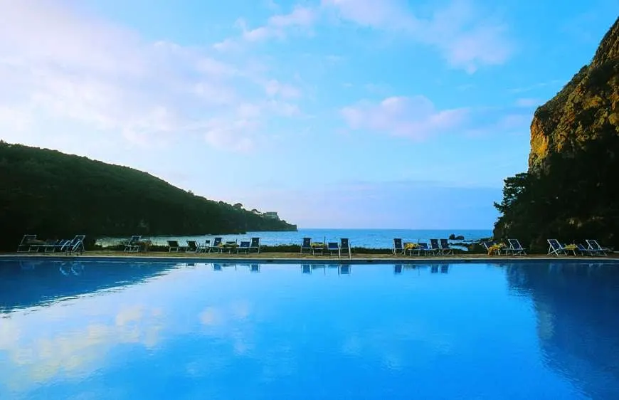A wide pool reflecting the sky, facing a wooded bay and the sea