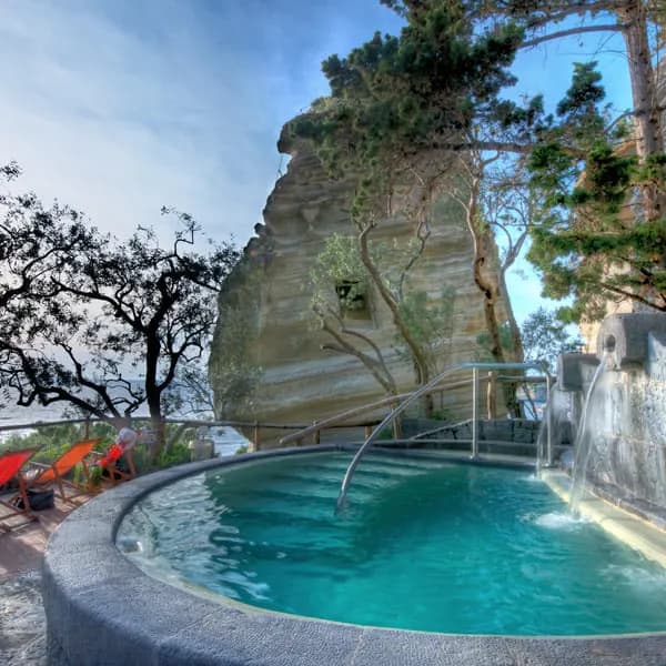 A steaming thermal pool with a fountain beside a tall sandstone rock