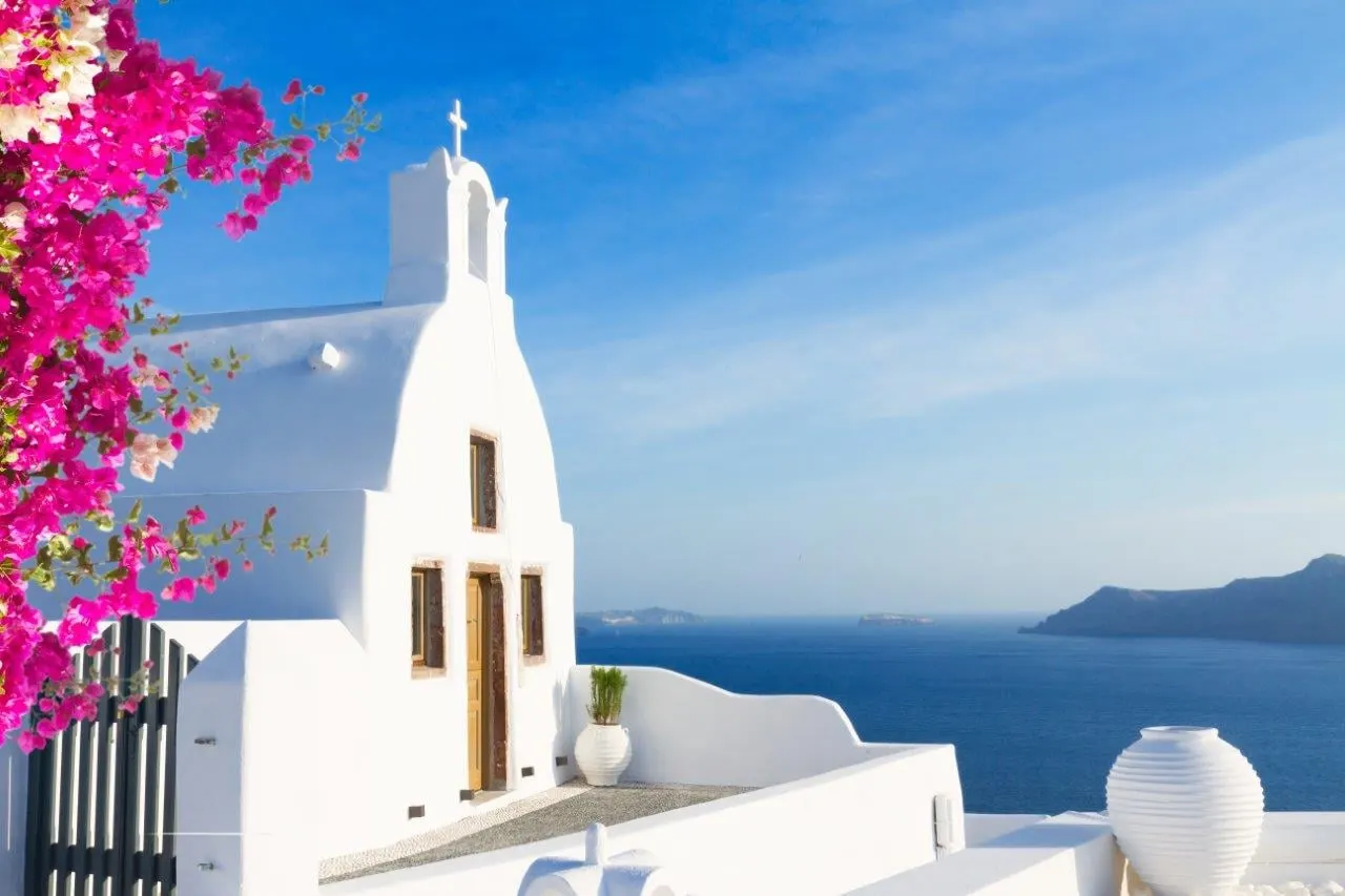 A white chapel with pink bougainvillea above the sea