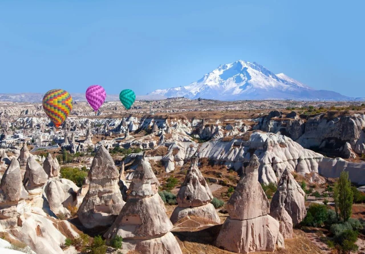 Hot air balloons over fairy chimneys with a snow-capped volcano behind