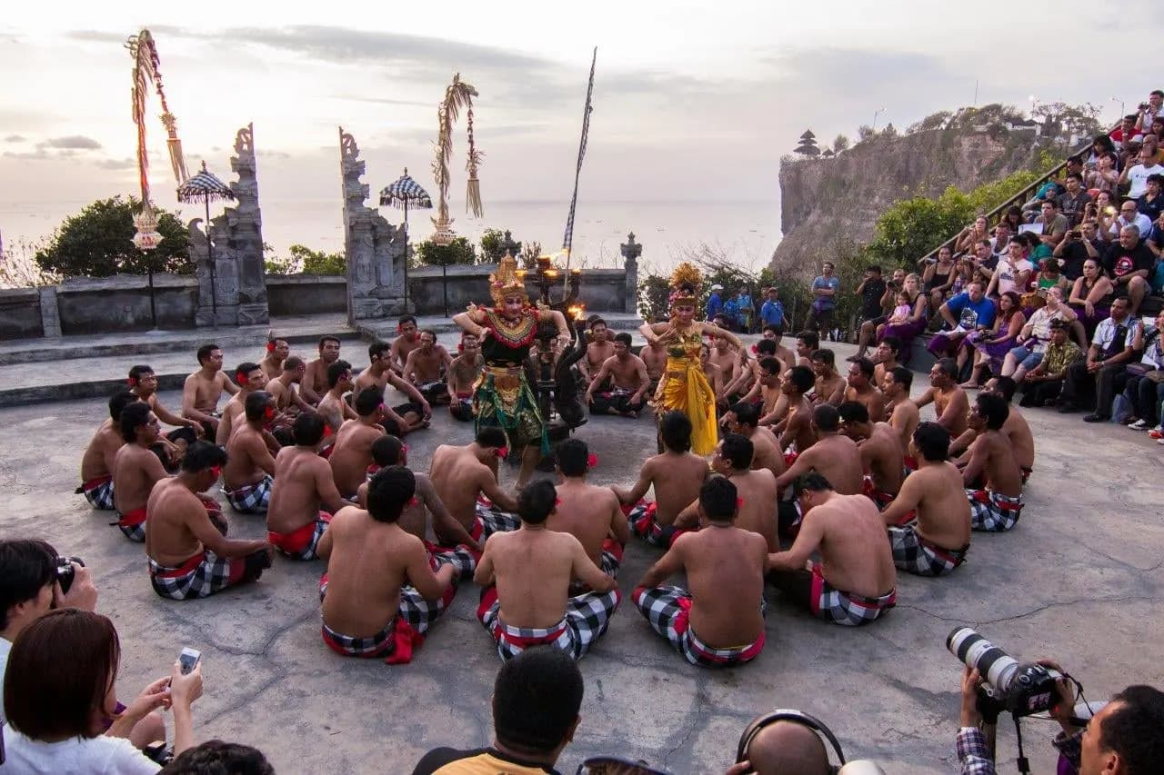 Kecak dancers seated in a circle on a clifftop stage at Uluwatu in the evening