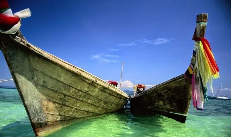 Two wooden longtail boats with ribbons on their bows in clear green shallows