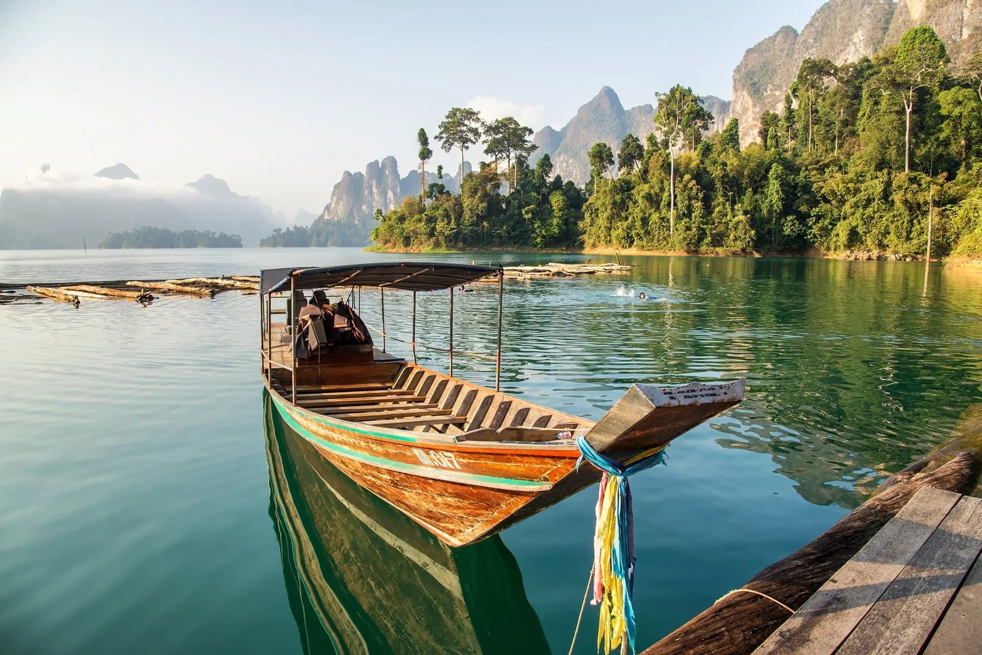 A painted long-tail boat moored on a calm lake with forested karsts behind