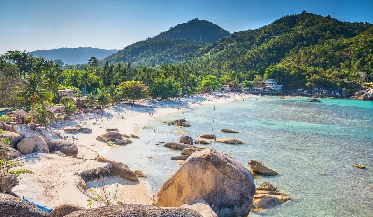 Granite boulders and a curving sandy bay below forested hills on Koh Samui