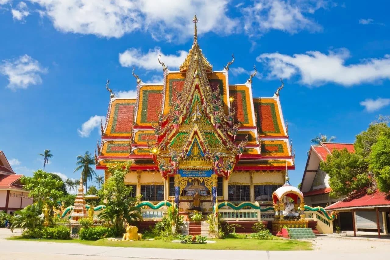 An ornate red and gold temple hall under a blue sky on Koh Samui