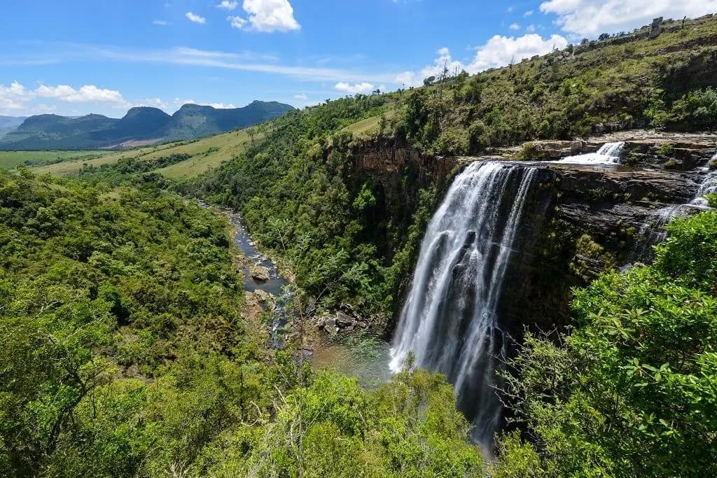 A waterfall dropping from a rock ledge into a forested gorge on the Panorama Route