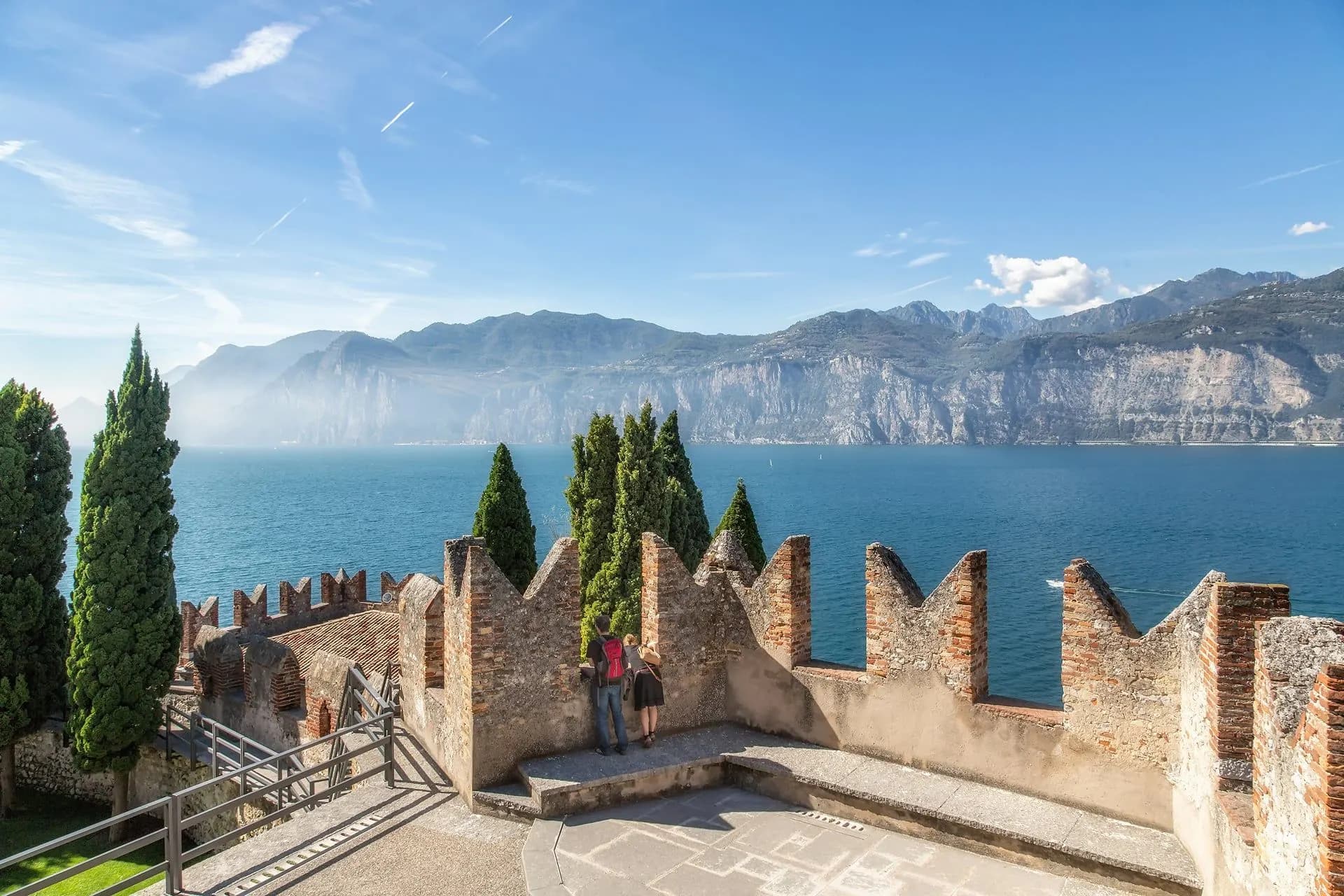 Castle battlements and cypresses above the blue water and mountains of Lake Garda