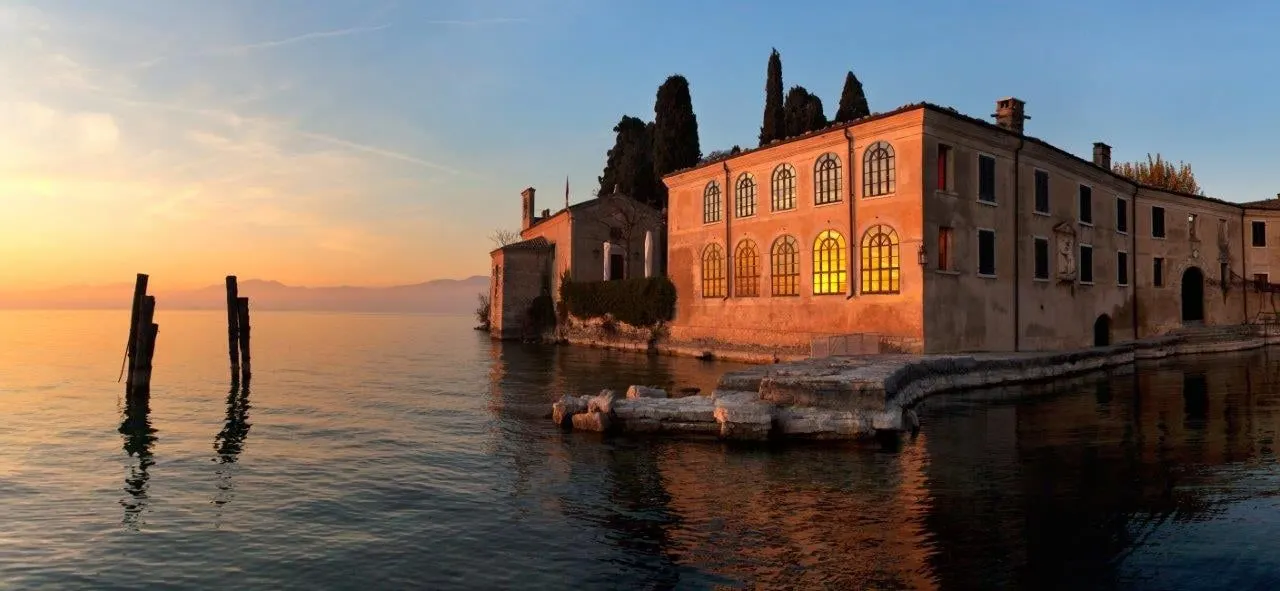 A lakeside villa and cypress trees glowing at sunset on Lake Garda
