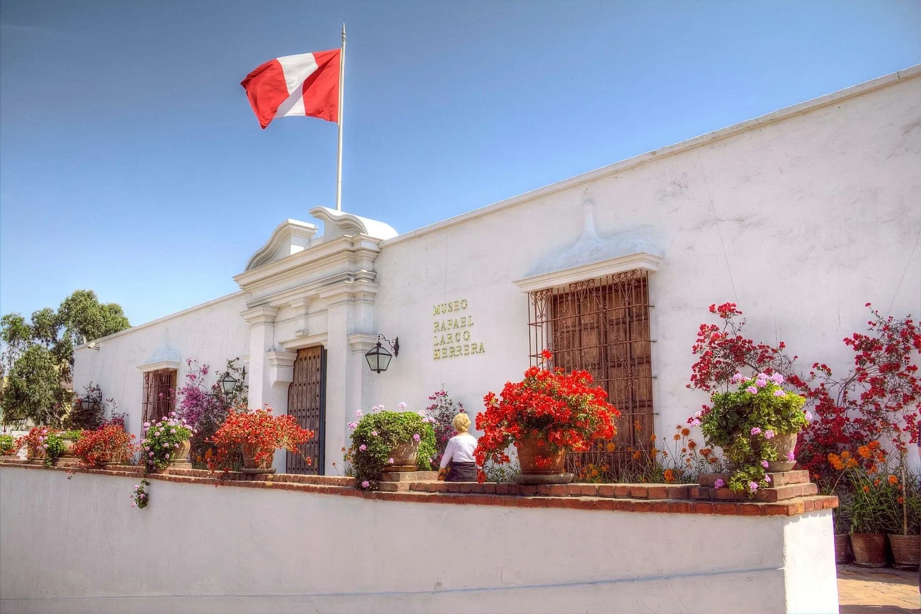 The white colonial mansion of the Larco Museum with red flowers and the Peruvian flag