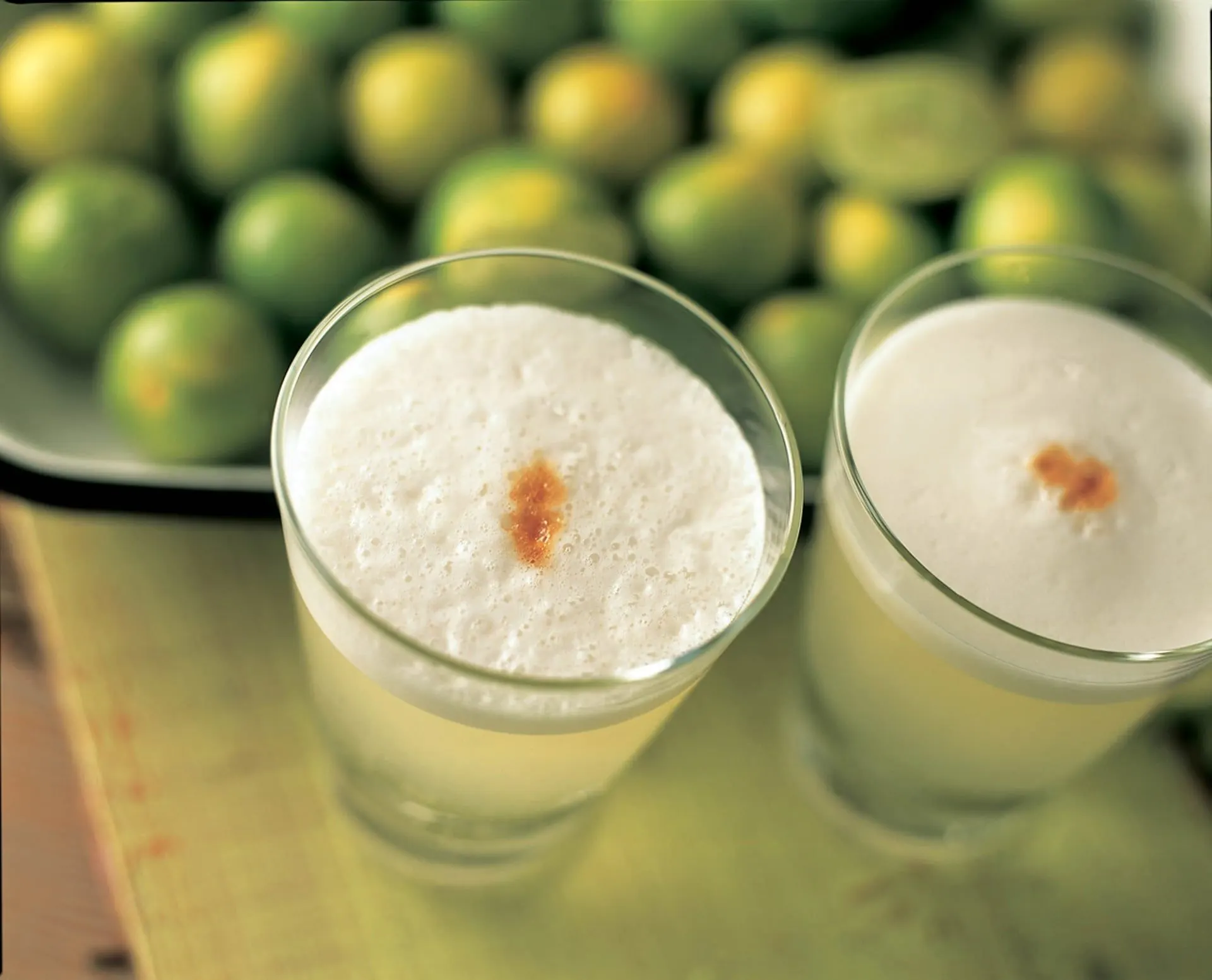 Two frothy pisco sours in front of a bowl of limes