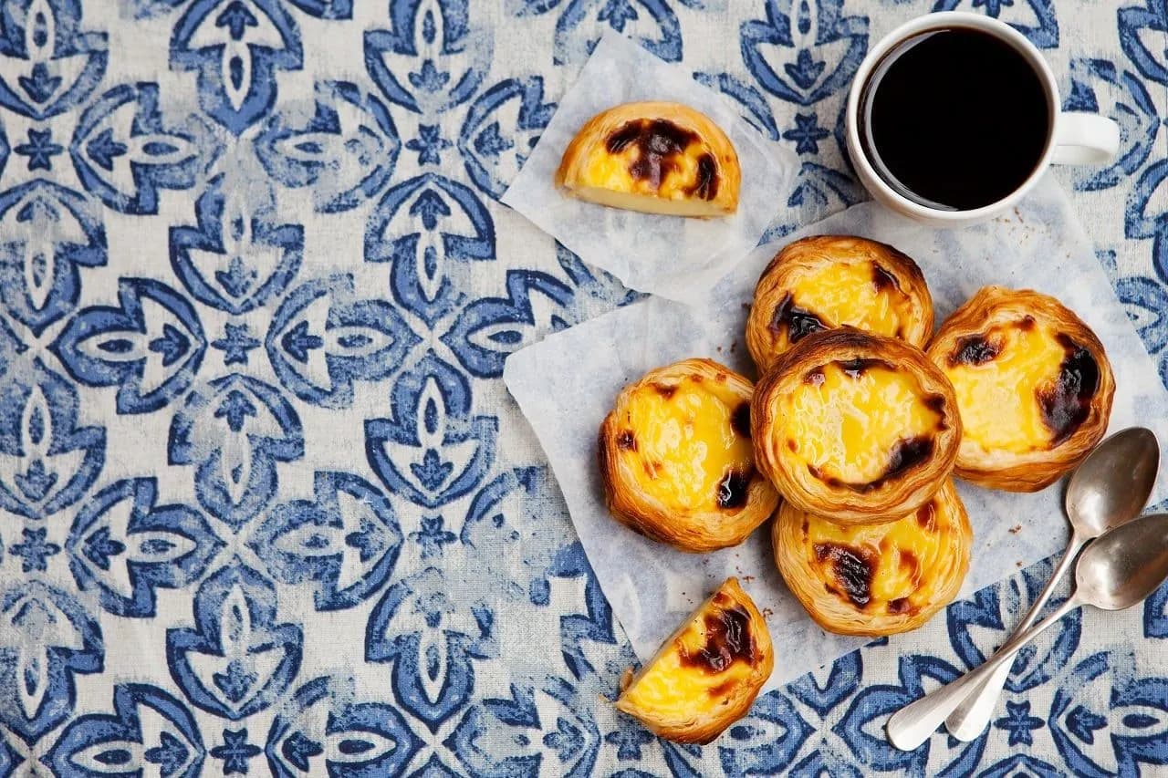 Portuguese custard tarts and a coffee on a blue and white tiled cloth