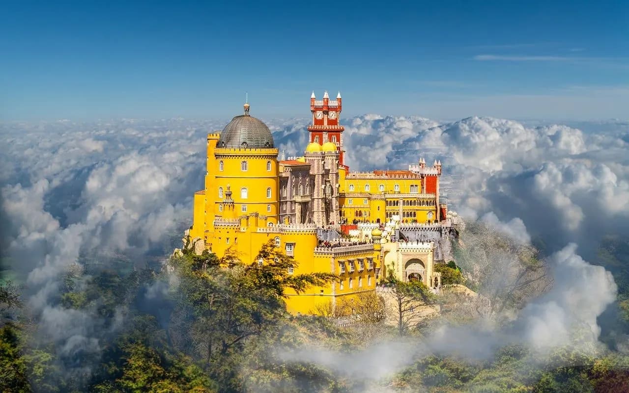 The yellow and red Pena Palace in Sintra rising above the clouds