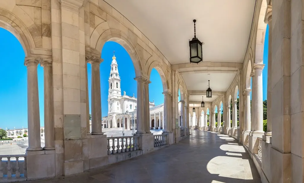 A shaded colonnade framing the bell tower of the Fátima basilica