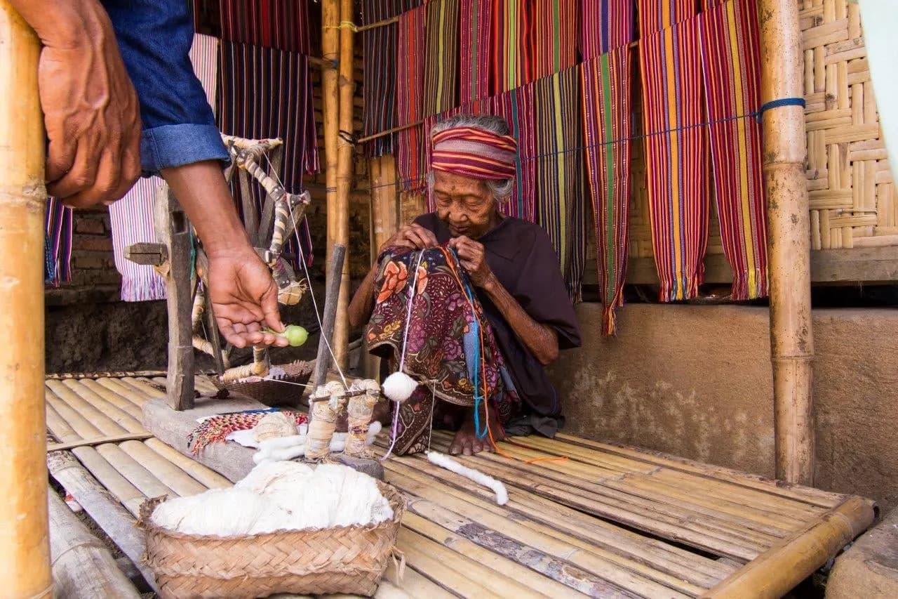 A village weaver at work beside hanging lengths of striped handwoven cloth
